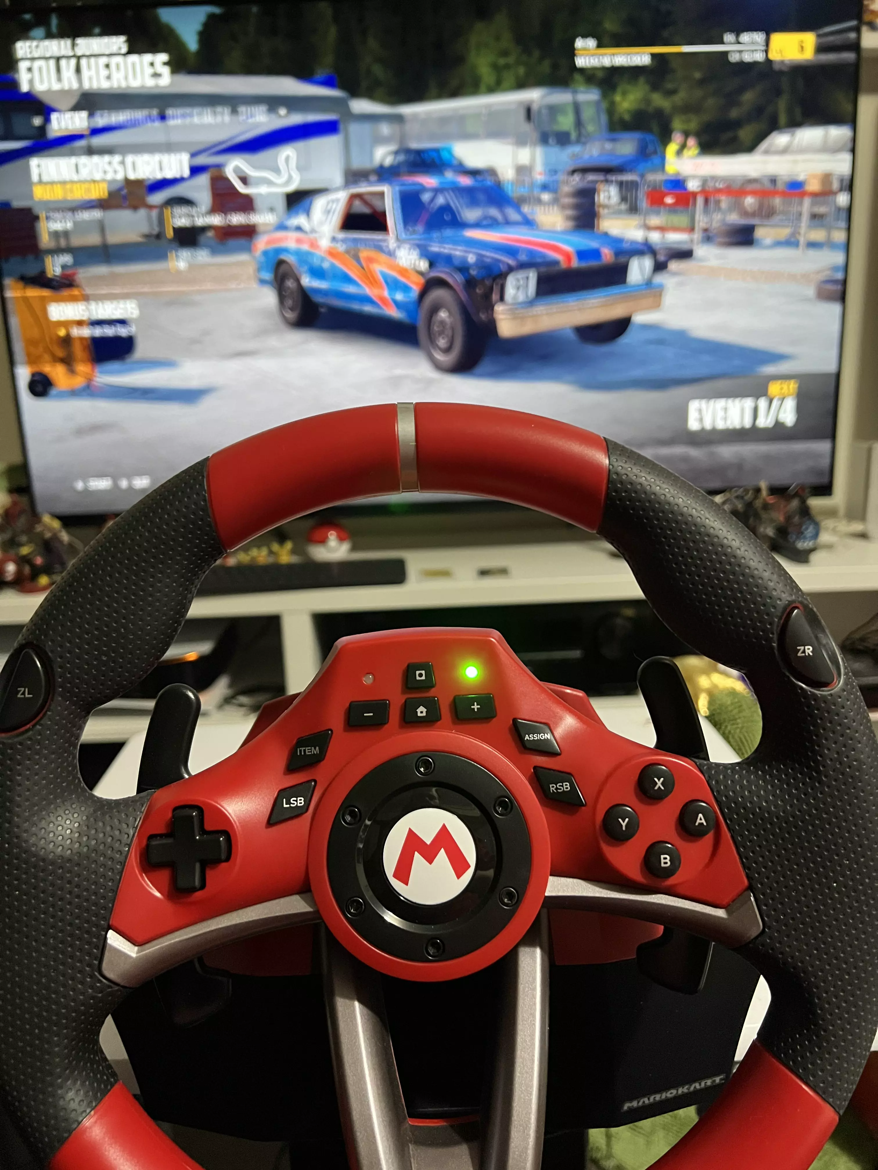 The HORI Mario Kart Racing Wheel Pro Deluxe, with Wreckfest on the TV behind